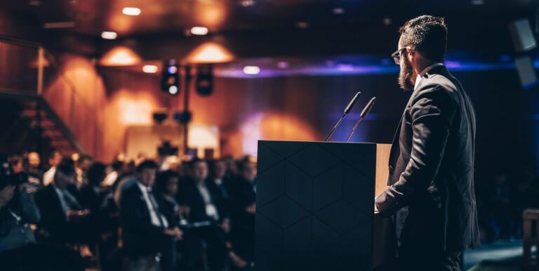 Photo of a speaker speaking in front of an audience